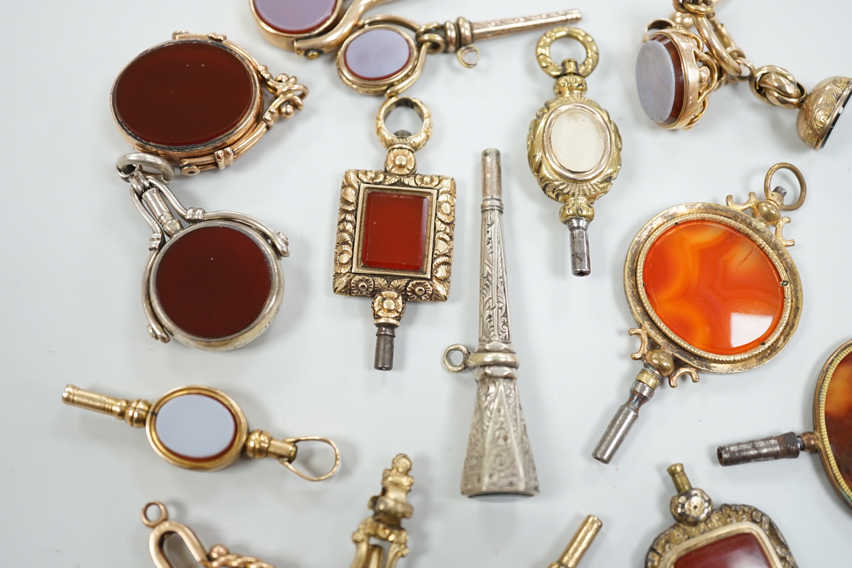 Sixteen assorted 19th century and later, 9ct gold and yellow or white metal overlaid and chalcedony set watch keys, including bloodstone, sardonyx, banded agate and moss agate and spinning fobs, largest 56mm.